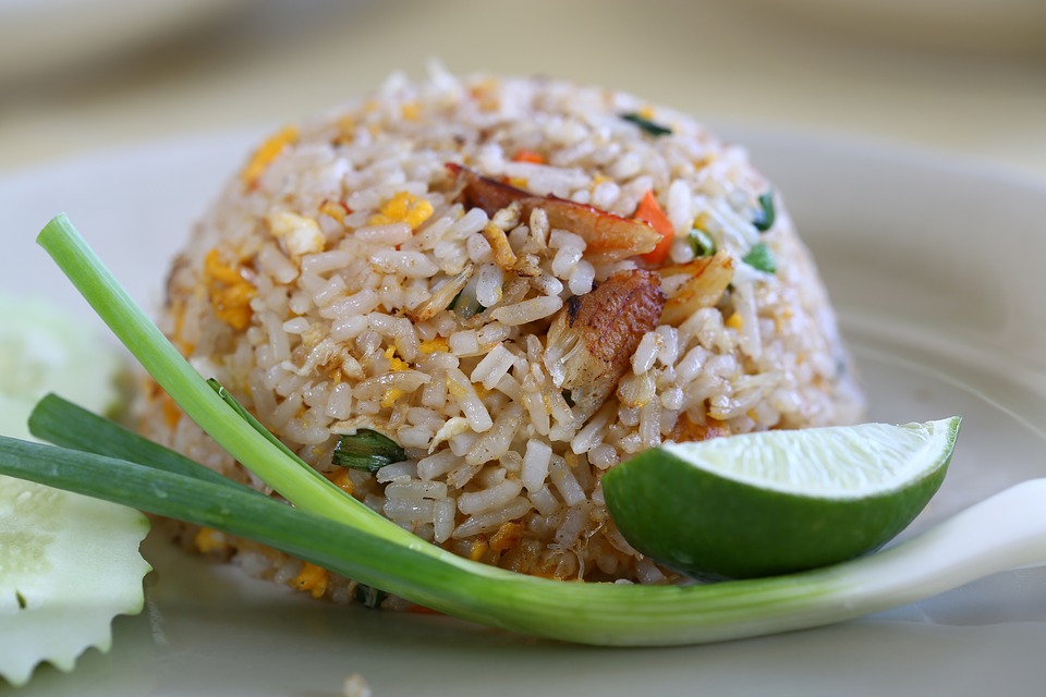 A plate of fried rice with egg, green onion, a wedge of lime and sliced cucumber